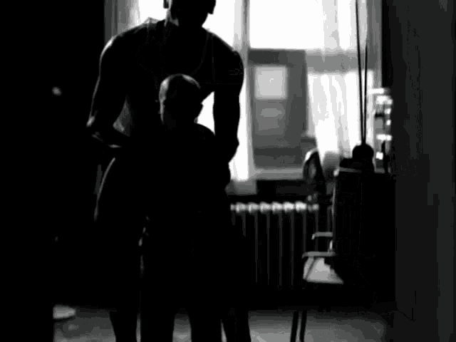 a black and white photo of a man standing in front of a window in a room .