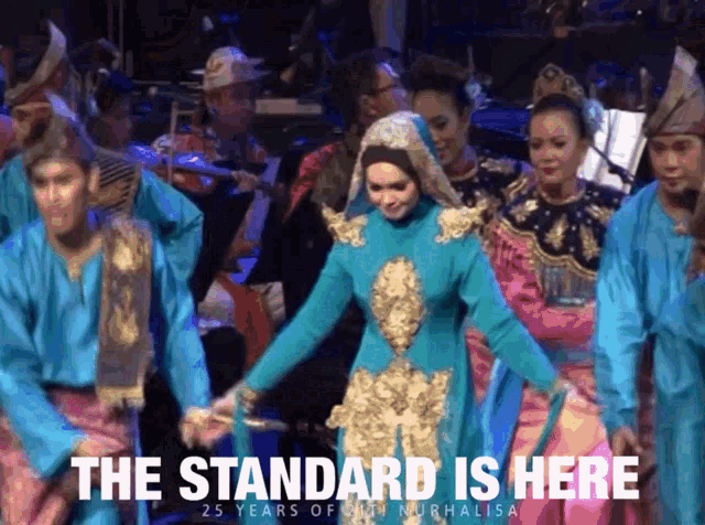 a woman in a blue dress is dancing in front of an orchestra with the words the standard is here