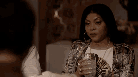 a woman is sitting at a table holding a glass of water and talking to another woman .