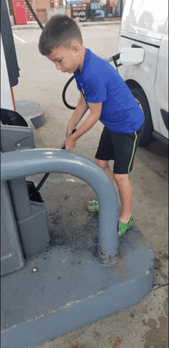 a young boy in a blue shirt is pumping gas