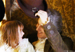 a man and a little girl are sitting on a couch and the little girl is looking at the man 's hat