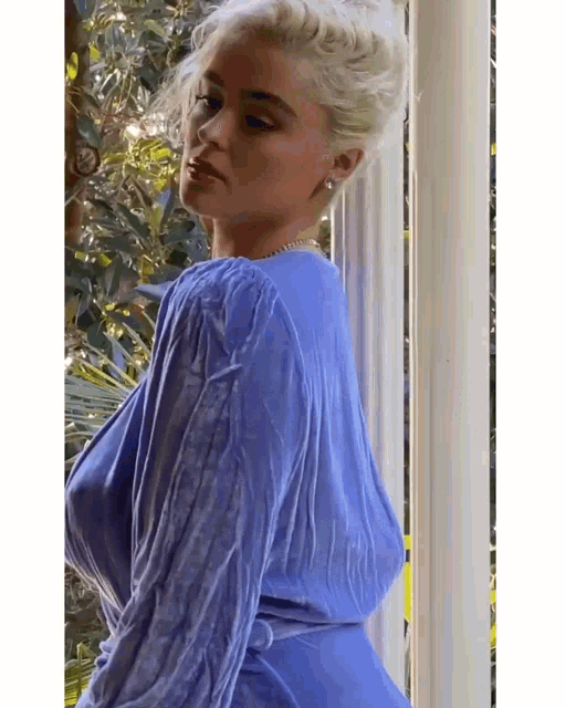 a woman in a blue dress is standing next to a window .