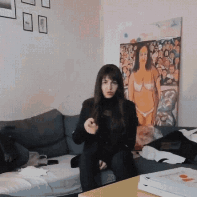 a woman is sitting on a couch in front of a painting