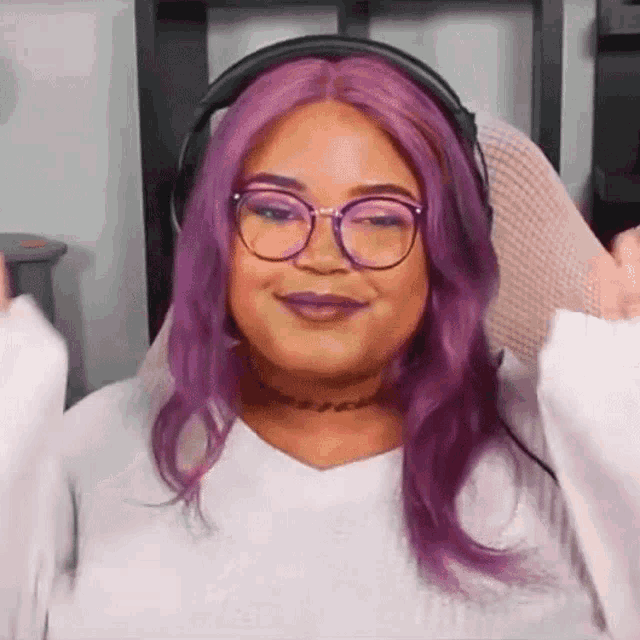a woman with purple hair and glasses is wearing headphones and making a funny face .