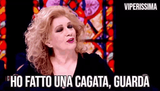 a woman with curly hair is sitting in front of a stained glass window and saying ho fatto una cagata guarda .