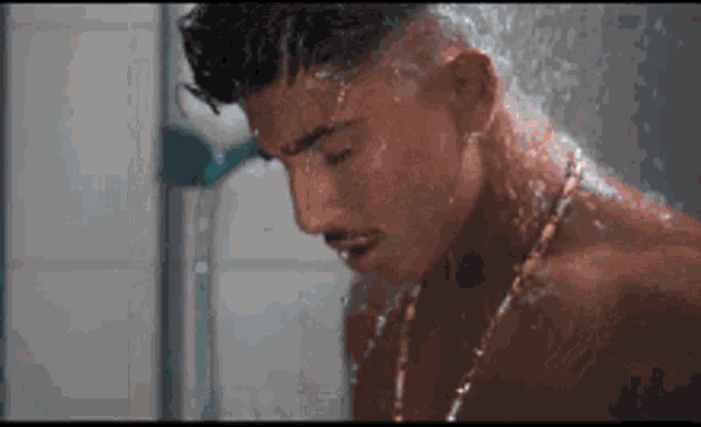 a shirtless man is taking a shower while wearing a necklace