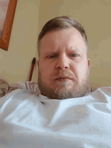 a man with a beard is laying on a bed with a blue shirt on