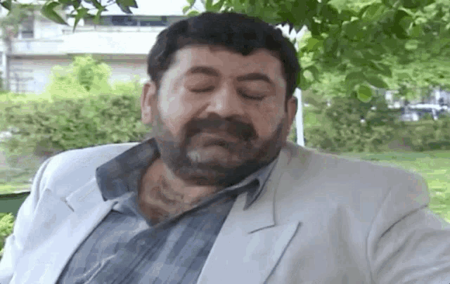 a man with a beard is sitting on a park bench with his eyes closed