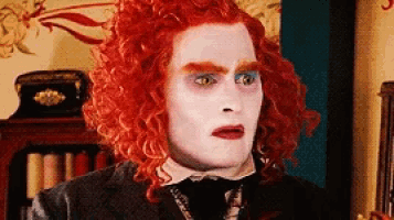 a man with red curly hair and white makeup is wearing a suit and tie .