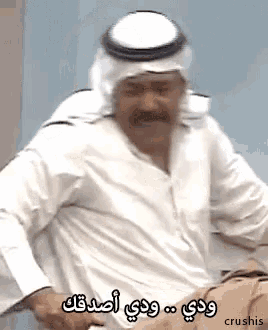 a man wearing a turban and a white shirt is sitting on a chair and making a funny face .