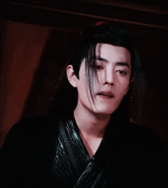 a man with long black hair is wearing a black jacket