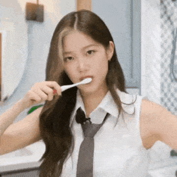 a young woman in a white shirt and tie is brushing her teeth .