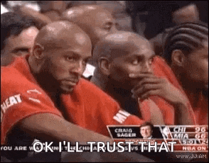 a group of men are sitting in a stadium watching a basketball game and one of them is covering his mouth with his hand .