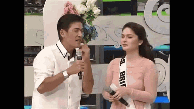 a man is talking into a microphone while a woman stands next to him holding a microphone .