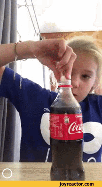a young girl is opening a coca cola bottle