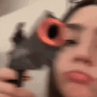 a woman is holding a toy gun in front of her face and pointing it at the camera .