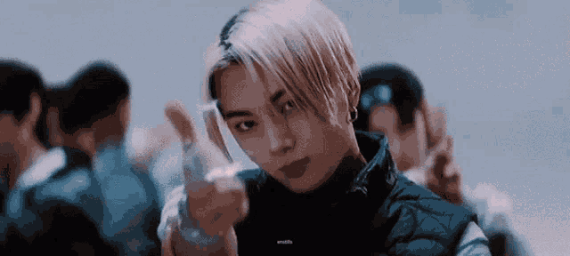 a young man with blonde hair is giving a peace sign while standing in a crowd .