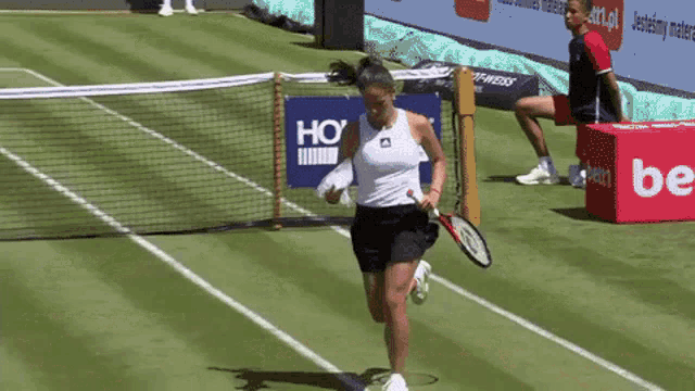 a woman holding a tennis racquet on a tennis court with a ho sign in the background