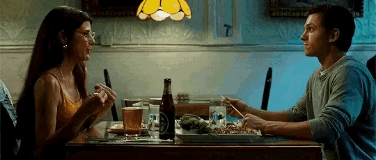a man and a woman are sitting at a table eating food and drinking beer .