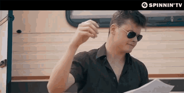 a man wearing sunglasses and a black shirt is holding a piece of paper in front of a trailer .