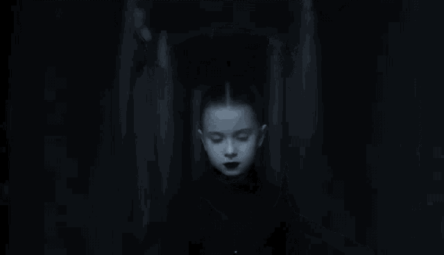 a little girl with black lipstick is standing in a hallway .