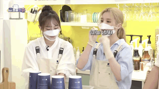 two women wearing aprons and face masks are standing in a kitchen
