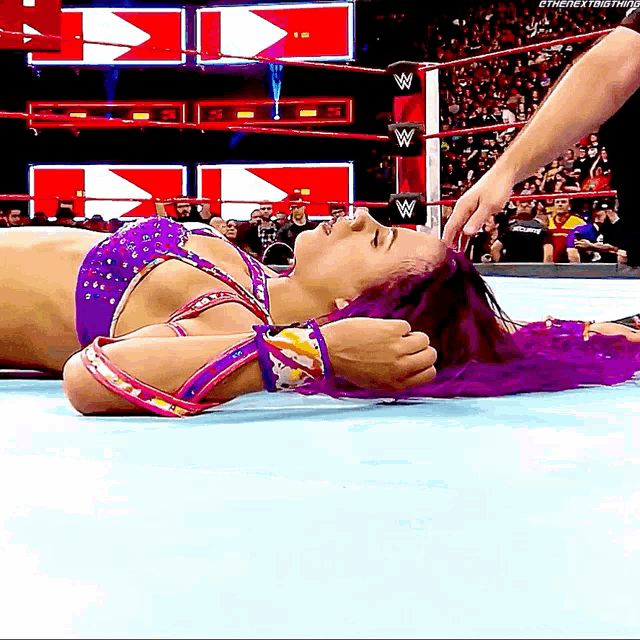 a woman with purple hair is laying on the ground in a wrestling ring while a man holds her hair