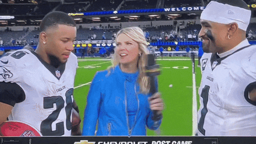 a woman with a microphone is talking to two football players one of whom has the number 20 on their jersey