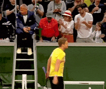 a man in a yellow shirt is holding a tennis racquet in front of a crowd that is clapping