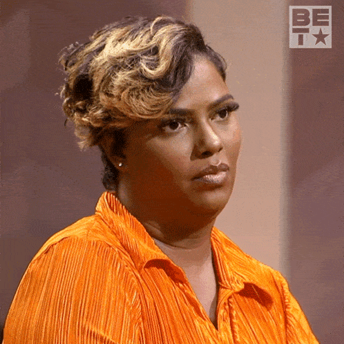 a woman in an orange shirt is standing in front of a be t logo