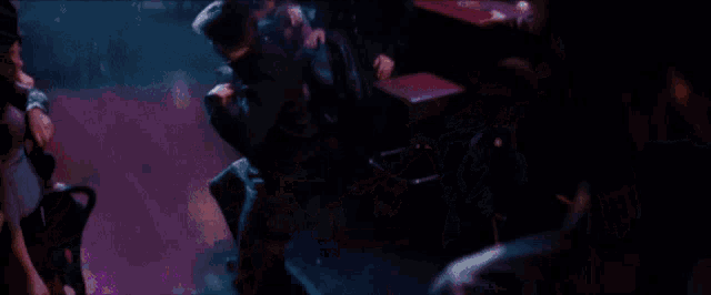 a group of people are dancing in a dark room with purple lights