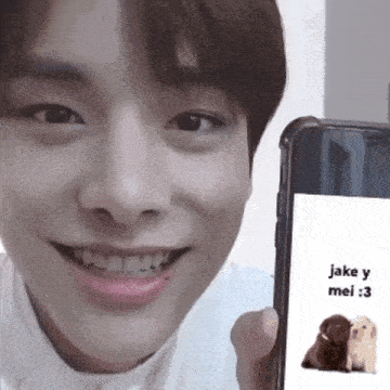 a young man is smiling while holding a cell phone with a picture of two dogs on the screen ..
