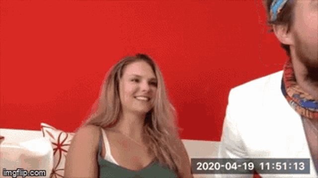 a man and a woman are sitting on a couch with a red wall behind them ..