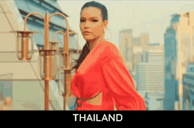 a woman in a red dress is standing in front of a city with the word thailand below her