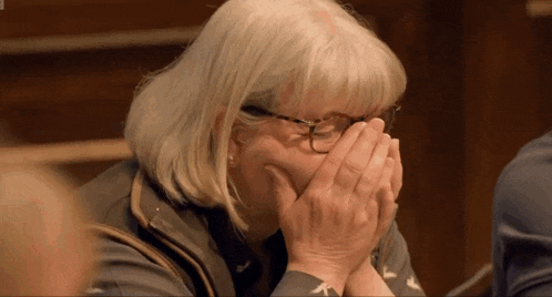 an older woman with glasses is covering her mouth with her hands .