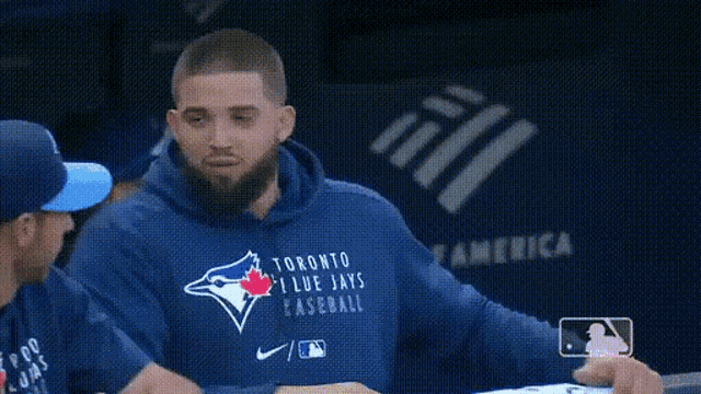 a man wearing a toronto blue jays sweatshirt is talking to another man .