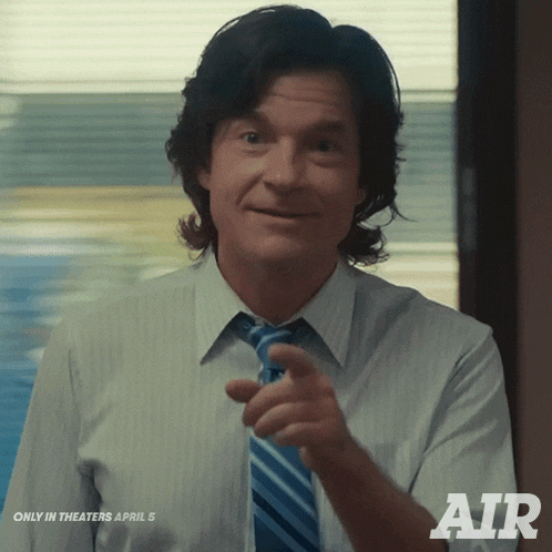 a man in a white shirt and blue tie is pointing at the camera with the word air behind him