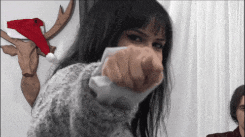 a woman in a sweater is holding a remote control in her hand and pointing at the camera .