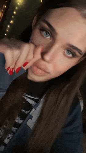 a woman with blue eyes and red nails is holding her nose