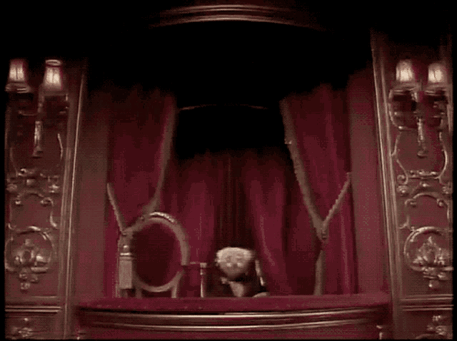 two muppets are sitting on a stage in front of red curtains