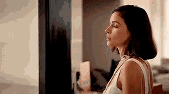 a woman in a white tank top is standing in front of a television in a room .