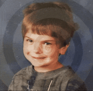 a young boy smiles for the camera with a blue background