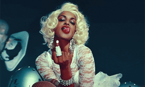 a woman in a blonde wig is sticking out her tongue and giving the middle finger