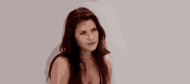 a woman with long hair is standing in front of a white wall and making a funny face .