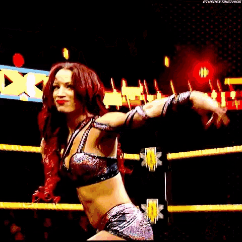 a woman with red hair is in a wrestling ring with her arms outstretched .