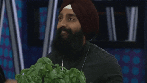 a man with a beard wearing a turban is sitting at a table with a bunch of green leaves .
