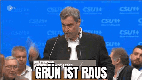 a man is giving a speech at a podium with the words grun ist raus written on a sign behind him .