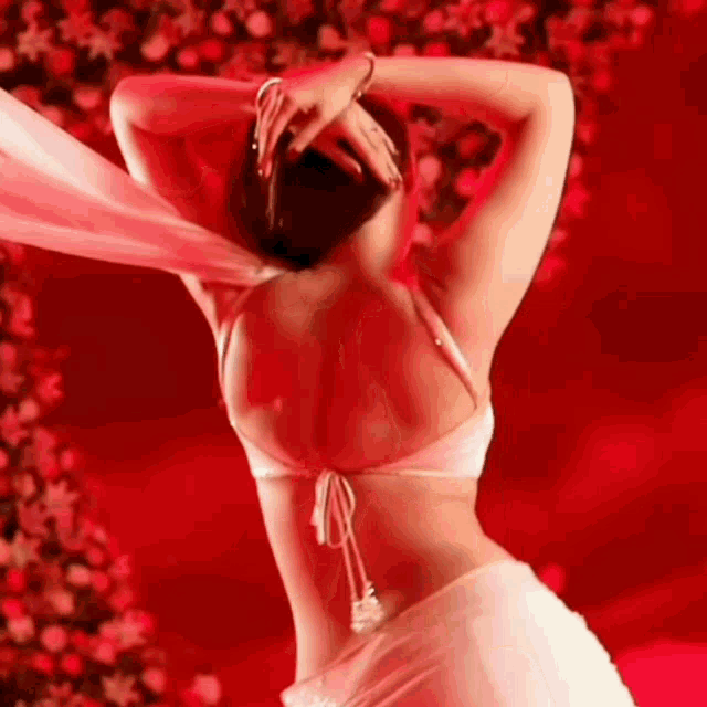 a woman in a white bra and white skirt is dancing in front of a red background