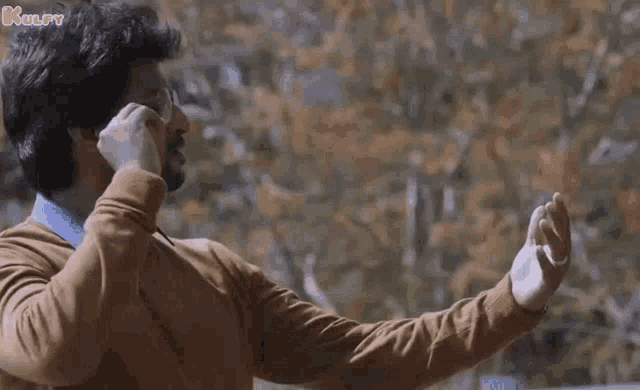 a man wearing glasses and a brown sweater is making a funny face with his hands outstretched .
