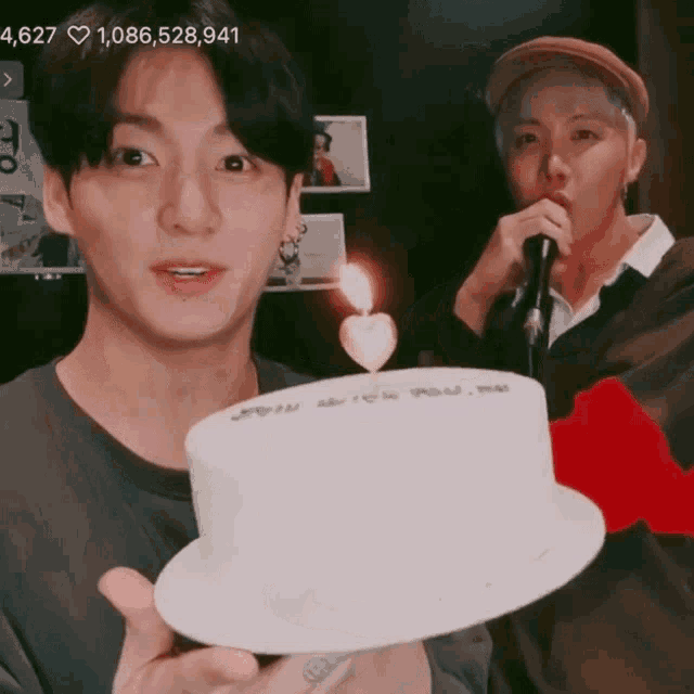 a man holding a cake with a heart shaped candle on it